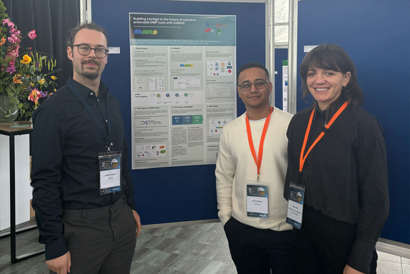 Two men and a woman standing in front of a poster wall with a poster.