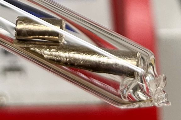 Eine durchsichtige Röhre, darin zwei messingfarbene Probenstückchen