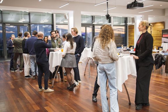 Blick in den Raum der Welcome Reception mit verschiedenen Studierenden, die sich in kleinen Gruppen unterhalten