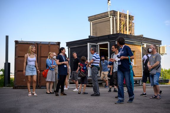 Die Besucher_innengruppe steht vor dem Freiluftprüfstand, an dem nachhaltige Baumaterialien getestet werden.