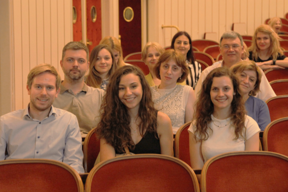 Besuch der Wiener Staatsoper. Die Personen sitzen im Zuschauer_innenraum. Mit rotem Samt bezogene Sessel.