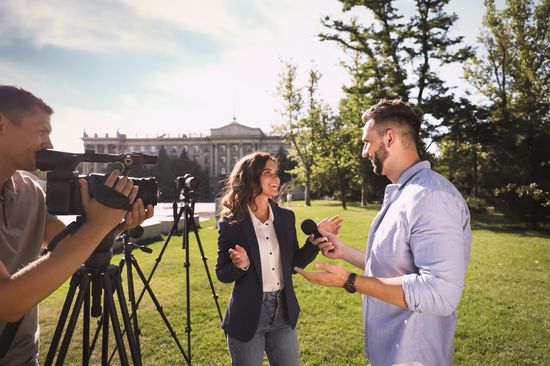 Das Foto zeigt eine Interviewsituation wischen einem Mann und einer Frau in einem Park, und mehrere Kameras, die auf die beiden Personen ausgerichtet sind.