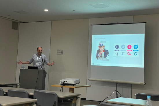 Das Foto zeigt eine männlicher Person an einem Rednerpult neben einer Leinwand mit Präsentation.