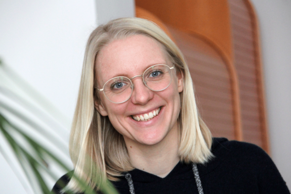 Dinah Gaffal, lächelnd, mit schwarzem Pullover, links im Vordergrund der verschwommene Zweig einer Palme.