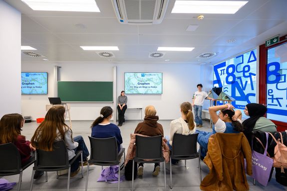 Raum mit Mädchen sitzend mit Blick zu Tafel und Monitor