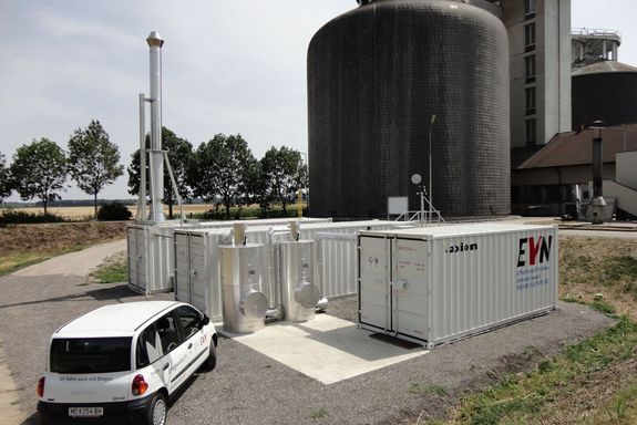 Eine Biogasanlge mit drei Containern (mit einem großen EVN Logo) im Vordergrund, vor denen ein Auto steht.