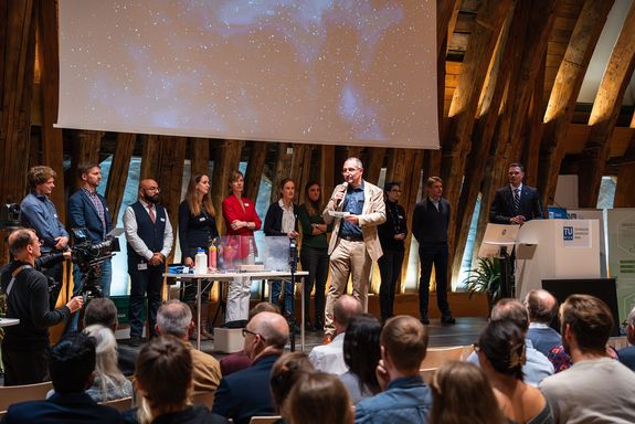 Bühne mit Personen sitzend Dekan Mihovilovic mit Mikrofon stehend