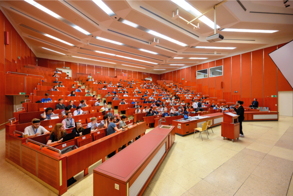 Lecture theatre with red walls, with audience and speaker