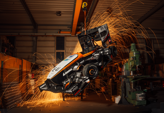 Rennauto in der Werkstatt aufgehängt, man sieht im Hintergrund Funken vom Schweißen