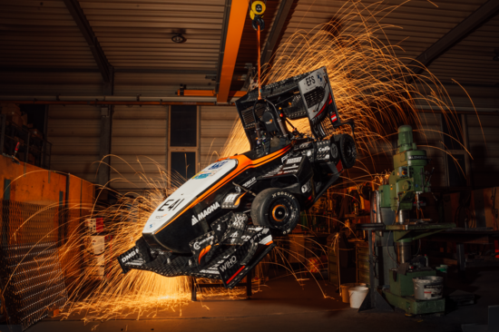 Rennauto in der Werkstatt aufgehängt, man sieht im Hintergrund Funken vom Schweißen 