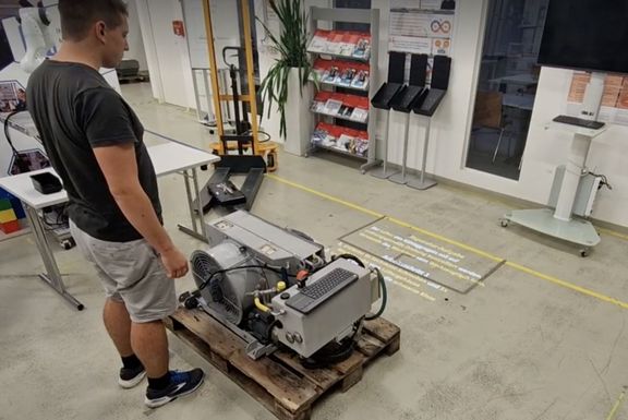 Mann in einer Fabrik vor einem Gerät, auf dem Boden projizierter Text