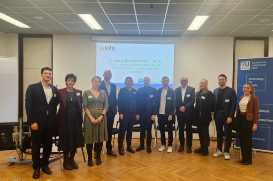 Gruppenfoto einiger Teilnehmer_innen einer Konferenz, die im leichten Halbkreis vor einem Screen stehen.