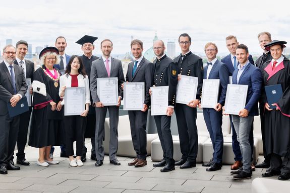 Preisträger_innen und Verbandsmitglieder nebeneinander aufgereiht. Die Preisträger_innen halten ihre Urkunden in den Händen.