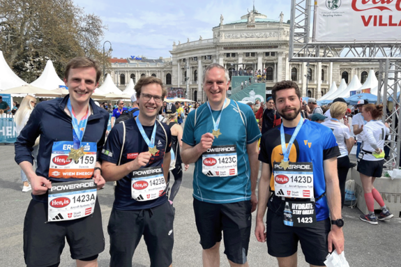 Vierköpfiges Marathonteam mit Medaillen am Wiener Rathausplatz. Im Hintergrund das Burgtheater.