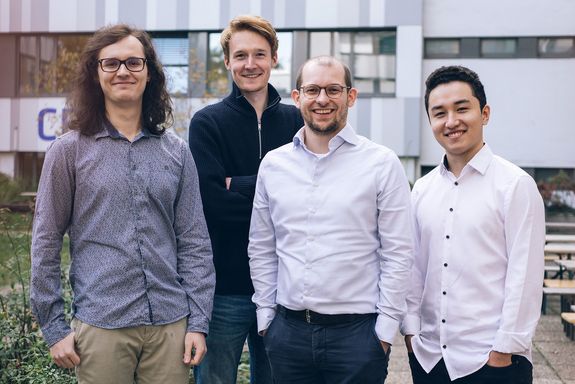 Gruppenfoto von vier Männern im Hemd, im Hintergrund eine Hausfassade