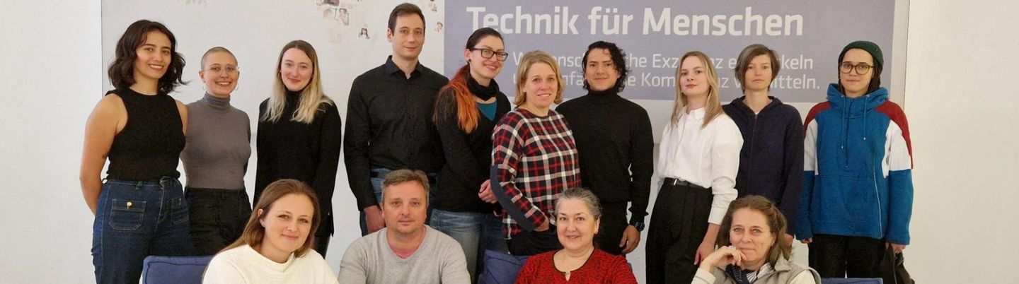 Mitglieder des Fachbereiches Forschungsinformationssysteme stellen sich zusammen für ein Foto auf. Im Hintergrund steht ein Plakat, das liest "Technik für Menschen".