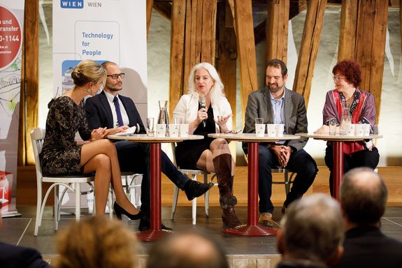 The presenter and the entire podium are seated on chairs on a raised platform. From left to right: Viktoria Raz, Florian Rudroff, Julie Rosser, Philipp Thurner and Ilse Gebeshuber.