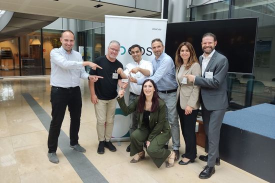 Eine Gruppe von sieben Personen steht vor einem EOSC-Roll-Up. Einige der Personen zeigen auf einen kleinen OSTrails-Aufkleber, den eine der Personen in der Hand hält.