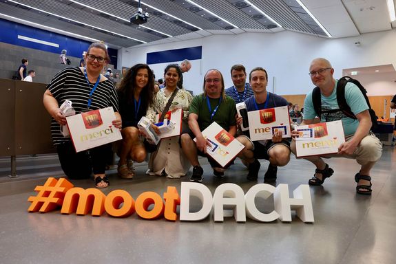 Menschen hockend hinter moot dach Schriftzug