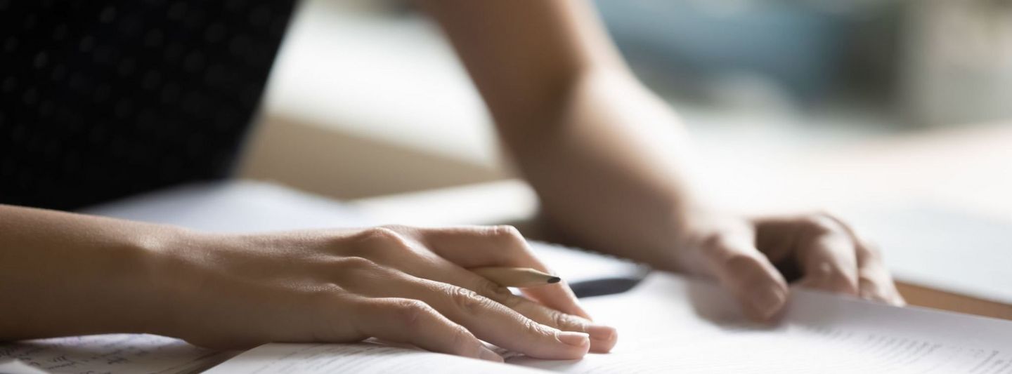 Close-up of a person holding a pen and reviewing documents or notes at a desk, suggesting focus and preparation.