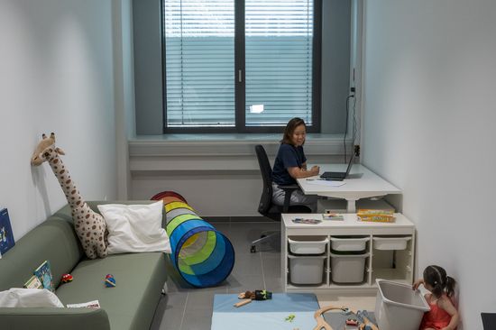 Eine Mutter arbeitet im neuen Eltern-Kind-Raum während das Kind am Boden spielt.