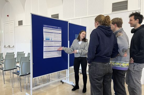 Gruppe von Interessent_innen stehen vor einer Tafel. Davor steht eine Frau, die Inputs zum Studium gibt