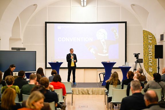 Rektor mit Mikro und Leinwand, davor Publikum sitzend