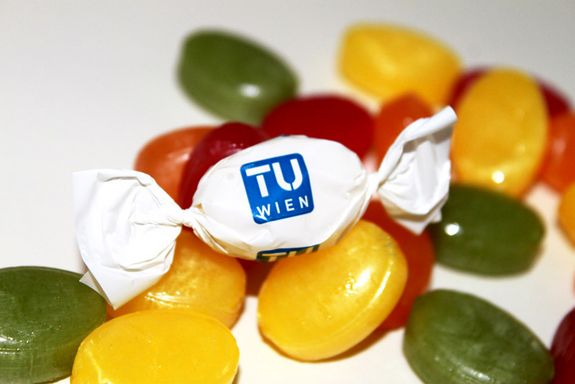 Ein bunter Haufen Zuckerl. Das in der Mitte ist in eine Verpackung mit TU-Logo gewickelt.