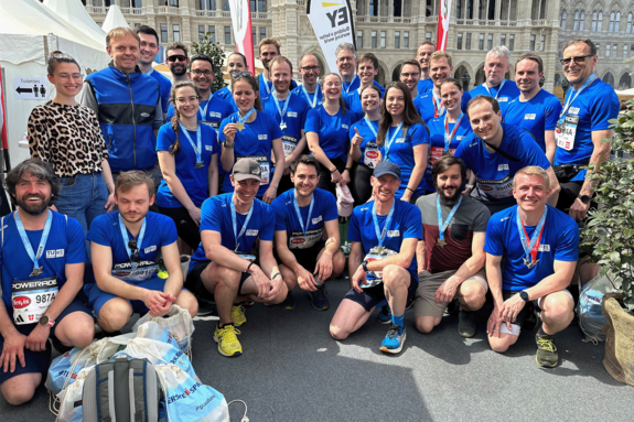 Gruppenfoto mit 36 Personen nach dem Marathon, teils hockend, teils stehend. Die Teilnehmer_innen tragen blaue T-Shirts und Medaillen.