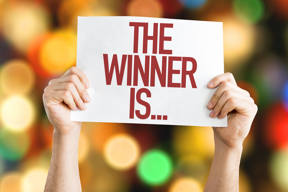 Hände halten Plakat "The Winner is ..." in die Höhe