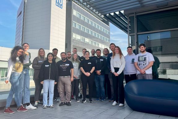 Gruppenfoto auf großer Terrasse. Im Hintergrund ein Gebäude mit TUW-Logo.