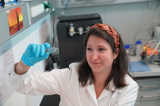 Wissenschafterin, die eine Probenmaterial auf einem Mikroskopieplättchen inspiziert.