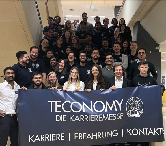 Gruppenfoto von jungen Menschen auf einem Stiegenaufgang - die 1. Reihe hält ein Banner mit "TECONOMY - die Karrieremesse: Karriere | Erfahrung | Kontakte" - daneben ist ein Logp