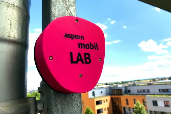 Eine Box mit der Aufschrift "aspern mobil lab" längt an einem Pfosten.