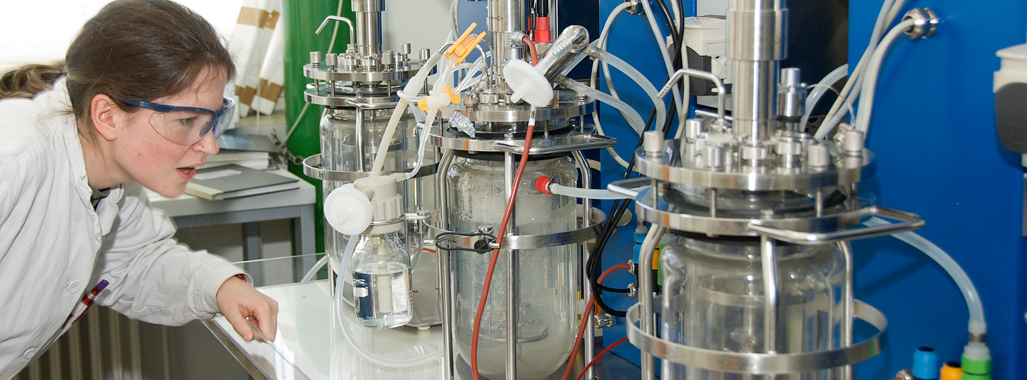 Studentin der Technischen Chemie im Labor. Sie steht vor Gläsernen Behältern.