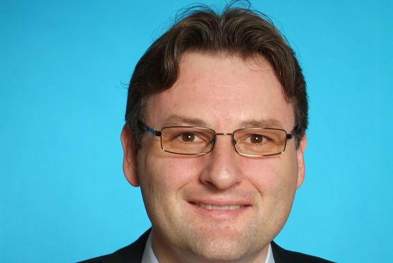 Andreas Kugi Portrait photo of Andreas Kugi on the bright blue background