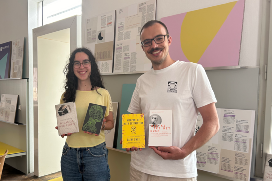 Two people hold the four books of the TU Wien Book Club up to the camera