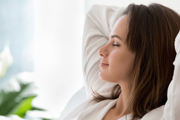 Frau in entspannter Haltung mit hinter dem Kopf verschränkten Armen. Bild in hellen Farben