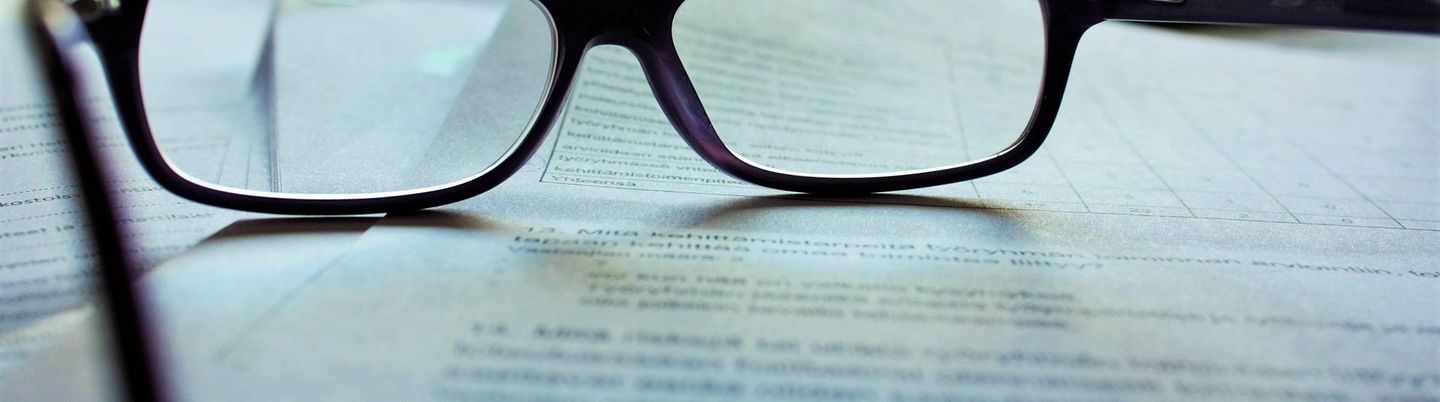 Eine schwarze Brille liegt auf Unterlagen
