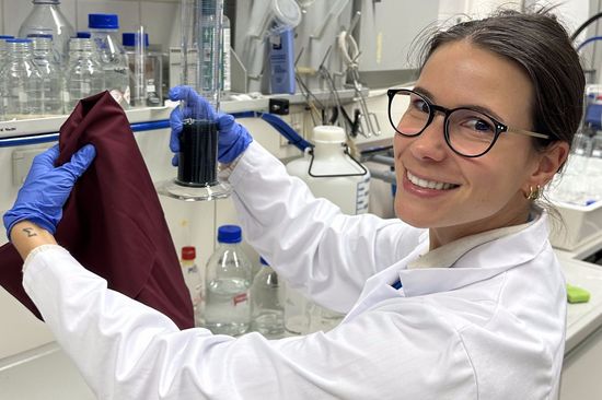 a woman in a white coat wearing safety goggles, holding a piece of cloth in a chemistry lab