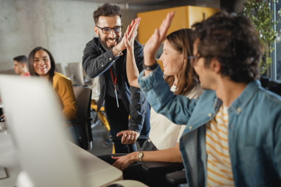 Vier Studierende sitzen vor Computer und klatschen sich ab