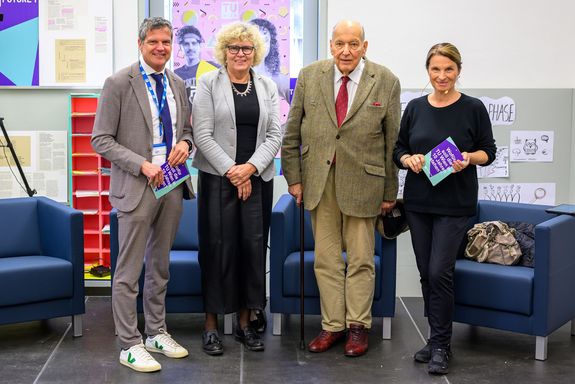 Gruppenbild mit vier stehenden Personen, vor Fauteuils.