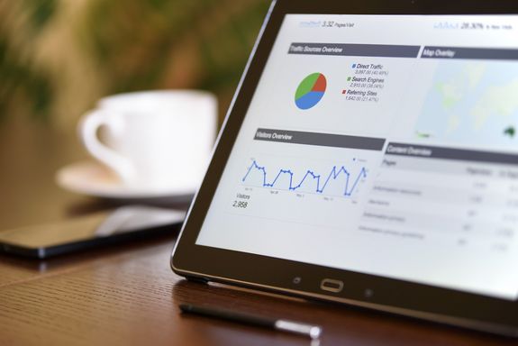 Foto eines Tablet-Bildschirms mit statistischen Daten auf einem Tisch, neben einem Handy und einer Kaffeetasse.