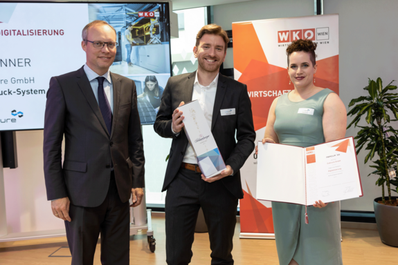 CEO Dr. Robert Gmeiner und Kathrin Wallner präsentieren eine Flasche Sekt und die MERCUR-Urkunde.