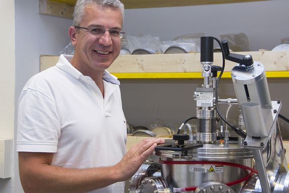 Prof. Paul Mayrhofer steht im Labor neben einer Apparatur und lächelt in die Kamera.