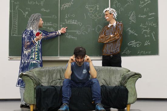 2 Männer stehen vor einer Tafel, auf der Formeln aus der Physik stehen. Der linke Mann hält einen Apfel in der Hand. Beide diskutieren eine Formel. Vor ihnen steht eine Couch, auf der ein Mann sitzt, der nachdenklich wirkt. 