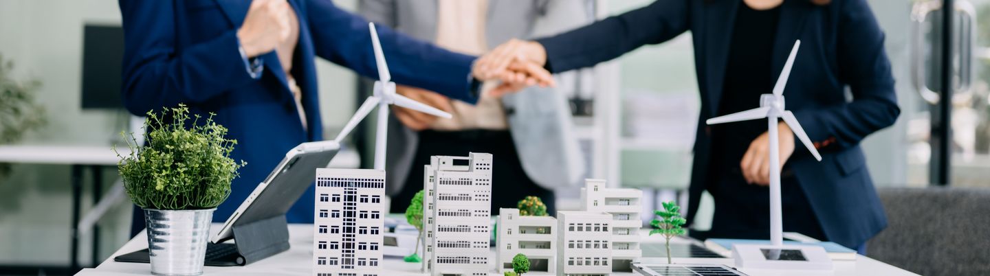 Group of diverse multiethnic businesspeople standing neare table looking at model of building from residential project. Green business company and Solar Energy Environment city