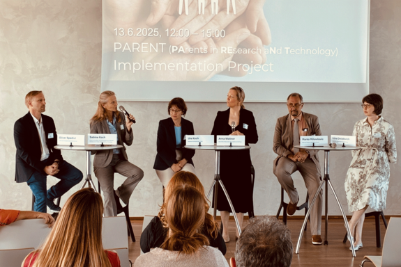 Diskussionsrunde mit Stehtischen und Screen im Hintergrund, sechs Personen