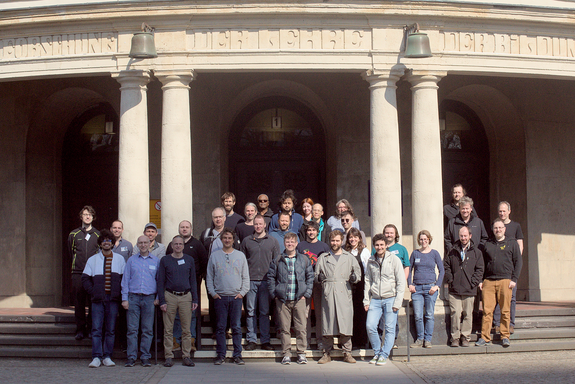 Das Foto zeigt eine Gruppe von etwa 30 erwachsenen Personen, die sich für das Foto auf den Stufen vor dem Eingang zu einem Gebäude aufgestellt hat.