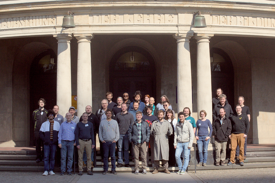 Das Foto zeigt eine Gruppe von etwa 30 erwachsenen Personen, die sich für das Foto auf den Stufen vor dem Eingang zu einem Gebäude aufgestellt hat.
